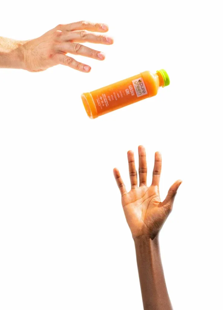 A hand catching a bottle of Pure Green cold-pressed juice